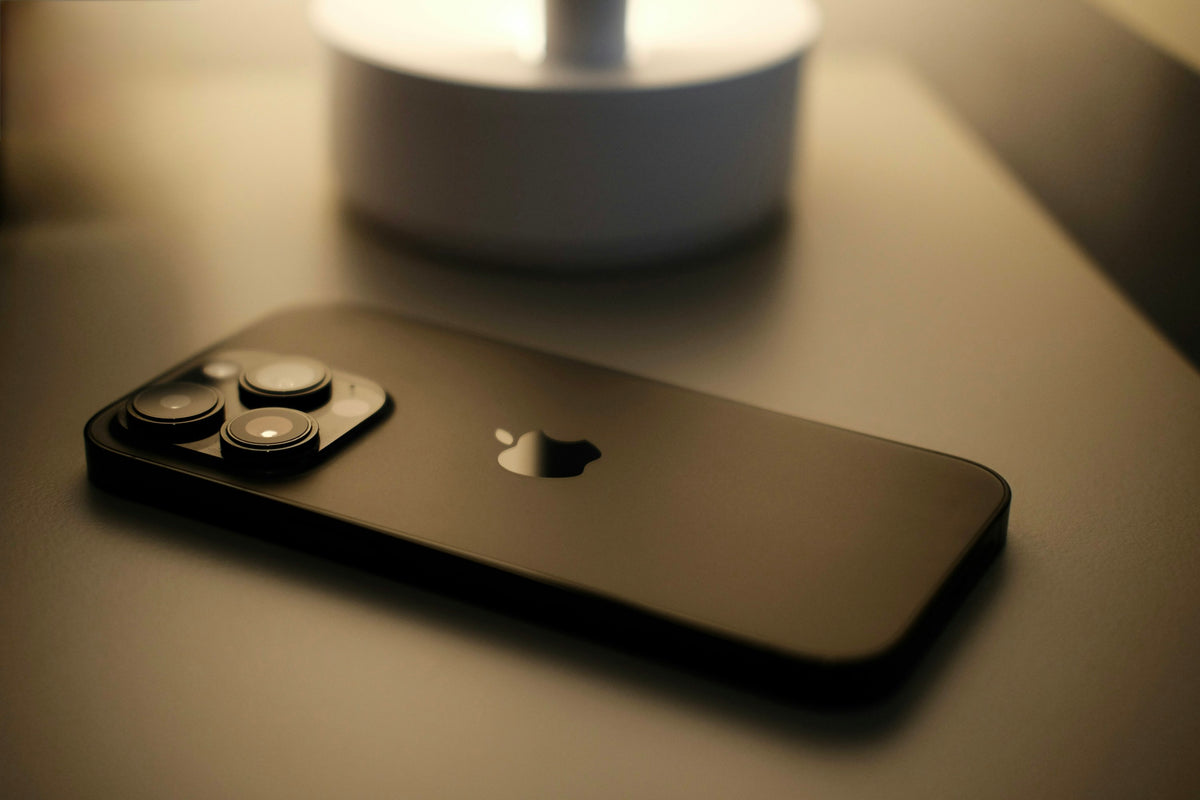 iPhone liegt abends auf dem Nachttisch neben einer Lampe